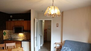A compact living space with a kitchenette, a dining area with wooden chairs, a grey sofa, and a hanging light fixture. - Ski-in/ski-out studio for 4, Place Emile Hodoul (Les Orres)
