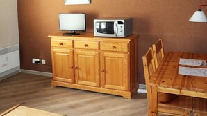 A wooden cabinet with a television and microwave on top, a dining table with chairs, and a wall-mounted light fixture. - Ski-in/ski-out studio for 4, Place Emile Hodoul (Les Orres)