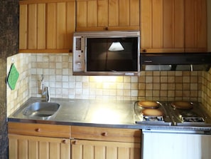 Cozinha com armários de madeira, micro-ondas, pia e fogão.