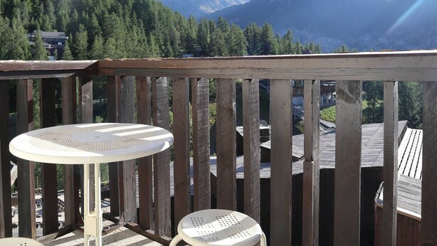 A wooden deck with a round table and a chair, overlooking a mountainous landscape with dense forests and a clear sky. - Ski-in/ski-out studio for 4, Place Emile Hodoul (Les Orres)