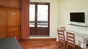 A room with wooden flooring, a bed, a dining table with chairs, a television mounted on the wall, and a sliding glass door leading to an outdoor area. - Studio for 4 in central Les Orres, near slopes (Les Orres)