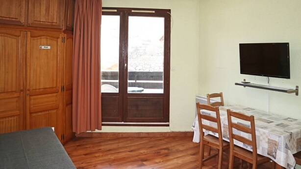 Une pièce dotée d’un plancher en bois, d’un lit, d’une table à manger avec des chaises, d’un téléviseur fixé au mur et d’une porte-fenêtre coulissante donnant sur un espace extérieur.