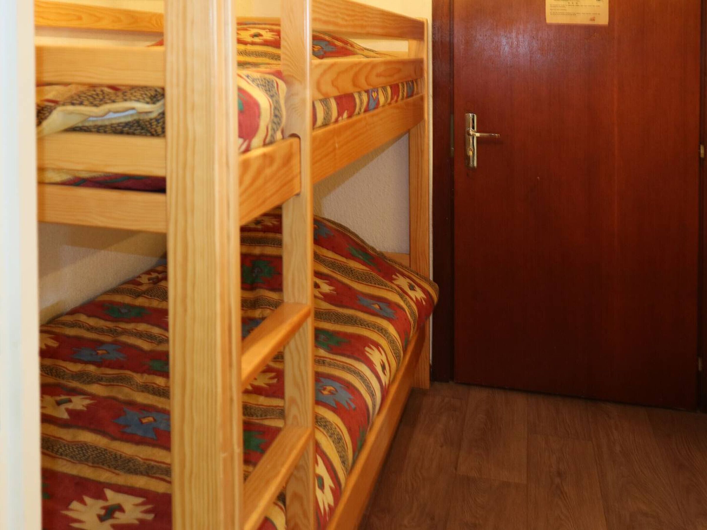 Een slaapkamer met stapelbed, een houten deur en een bed met een patroon.