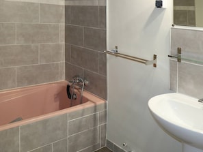 Un baño con bañera, lavamanos y estante de vidrio.