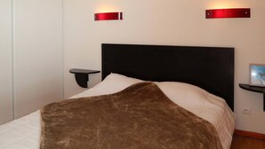 Quarto com cabeceira preta, colcha branca e manta marrom. Há duas mesas de cabeceira com iluminação vermelha.