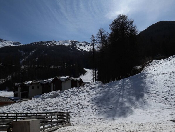 Paisaje montañoso cubierto de nieve con una valla de madera y edificios en primer plano.