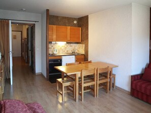 A compact kitchen with wooden cabinets, a tiled backsplash, and a dining area with a wooden table and chairs.