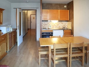 A compact kitchen with wooden cabinets, a tiled backsplash, and a dining area with a wooden table and chairs.