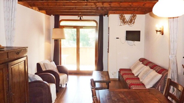 A cozy room with a wooden ceiling, a sofa, a dining table, and a TV mounted on the wall. - Spacious 2-room apartment for 6 in the center with balcony, washer (Les Orres)