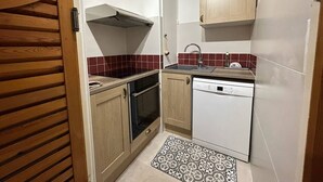 A compact kitchen with wooden cabinets, a built-in oven, a dishwasher, and a red-tiled backsplash. - Spacious 2-room apartment for 6 in the center with balcony, washer (Les Orres)