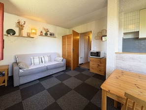 Un espace de vie compact comprenant un canapé, un meuble en bois, un four à micro-ondes et une petite table à manger.