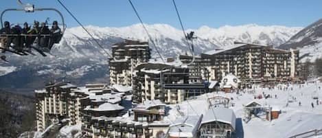 En skidort med flera byggnader, inklusive ett stort hotell med balkonger, skidliftar och en snötäckt bergskuliss.