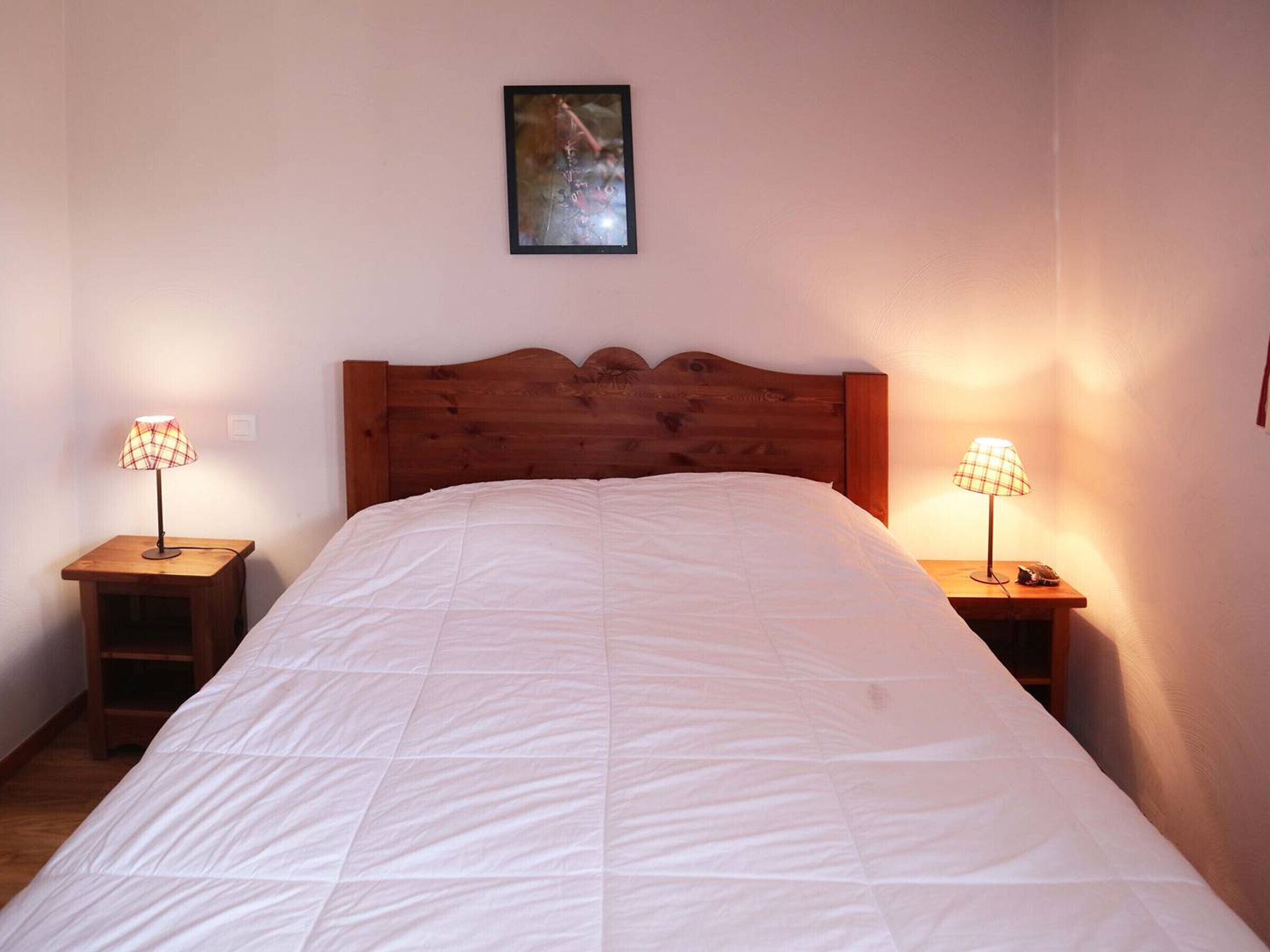 A bedroom with a wooden headboard, a white quilted bedspread, and two bedside lamps with a checkered lampshade.