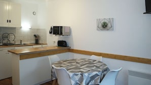Una cocina compacta con armarios blancos, un microondas y una pequeña mesa de comedor con sillas.