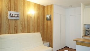Un espacio habitable compacto con un sofá blanco, una pequeña mesa de comedor y una zona de kitchenette.