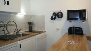 Cocina compacta con lavavajillas, microondas y pileta. Hay dos guantes de horno negros colgados en la pared.