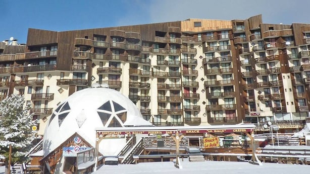 Un hotel de varios pisos con balcones, una gran estructura en forma de cúpula al frente y letreros que indican un restaurante y bar de aperitivos.