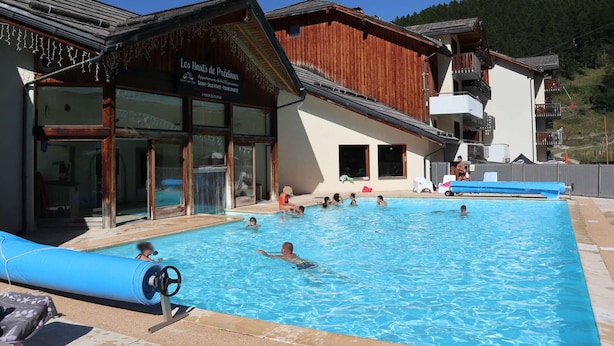 A swimming pool area with a wooden building labeled "Les Hauts de Préalux" and a mountain in the background. - Cozy Apartment for 8 with Pool, Sauna, and Ski-In/Ski-Out Access in Les Orres 1800 (Les Orres)