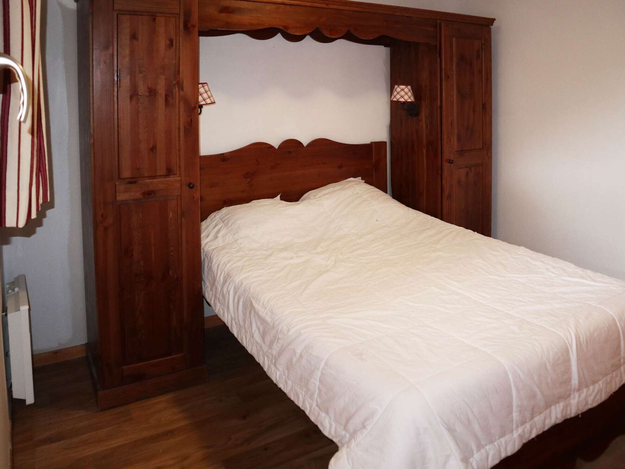A single bed with a wooden headboard and a white bedspread in a room with wooden walls and a door.