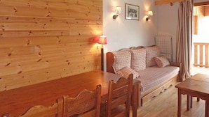 A cozy room with a wooden wall, a sofa with patterned cushions, a dining table with chairs, and two wall-mounted lamps. - Cozy Apartment for 8 with Pool, Sauna, and Ski-In/Ski-Out Access in Les Orres 1800 (Les Orres)