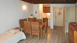 A cozy room with a bed, a dining table with wicker chairs, a kitchenette, and a door leading to another room. - Central Apartment, Ski-in/Ski-out, Sleeps 6, Balcony, South-Facing (Les Orres)
