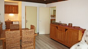 A cozy room with a wooden dining table, wicker chairs, a wooden cabinet, and a white sofa with star patterns. - Central Apartment, Ski-in/Ski-out, Sleeps 6, Balcony, South-Facing (Les Orres)