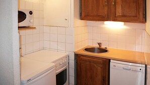 A compact kitchen with white appliances, wooden cabinets, and a tiled backsplash. - Central Apartment, Ski-in/Ski-out, Sleeps 6, Balcony, South-Facing (Les Orres)