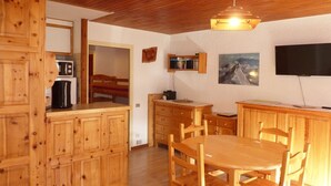 A wooden kitchen with a dining table and chairs, a microwave, a coffee maker, and a painting on the wall.