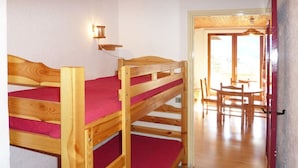 A bunk bed room with a wooden floor, a red mattress, and a wall-mounted light fixture.