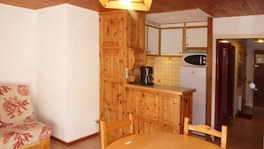 A cozy room with a wooden dining table, a chair, a small kitchenette with a microwave, and a cabinet.