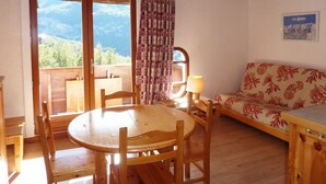 A cozy room with a wooden table and chairs, a sofa, and a view of mountains through a large window.