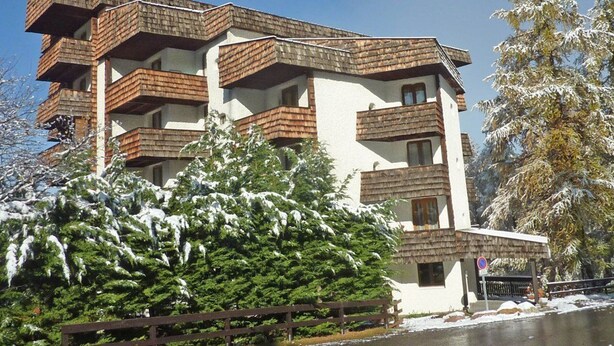 A multi-story building with balconies, surrounded by snow-covered trees and a clear sky.