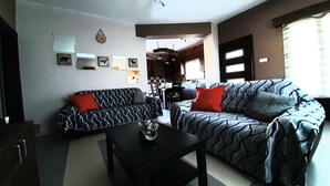 A living room with a sofa and armchair, a coffee table, and a dining area in the background.