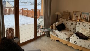 Una sala de estar acogedora con un sofá, una mesita y vistas a montañas nevadas a través de un ventanal.