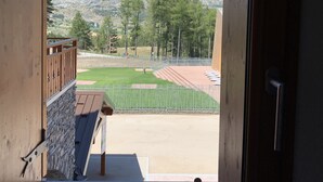 Vista desde una habitación con balcón de madera que da a un campo deportivo y montañas.