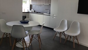 Una cucina moderna con mobili bianchi, una lampada a sospensione nera e una zona pranzo con tavolo rotondo e sedie bianche.
