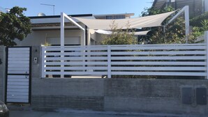 Un cancello chiuso con una recinzione bianca, un muro in cemento e un cancello in metallo.