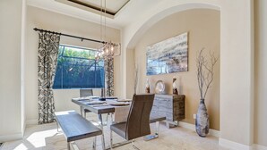 A dining area with a table set for two, a bench, a vase, and a painting on the wall.