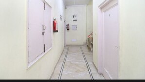 A narrow hallway with white doors on both sides, a fire extinguisher on the left, and a red railing on the right.