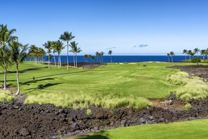 Un parcours de golf offrant une vue sur l’océan, entouré de palmiers et de formations rocheuses volcaniques.