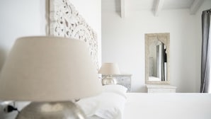 Een keurig opgemaakt bed met een lamp, een kaptafel met spiegel en een decoratief object aan de muur.