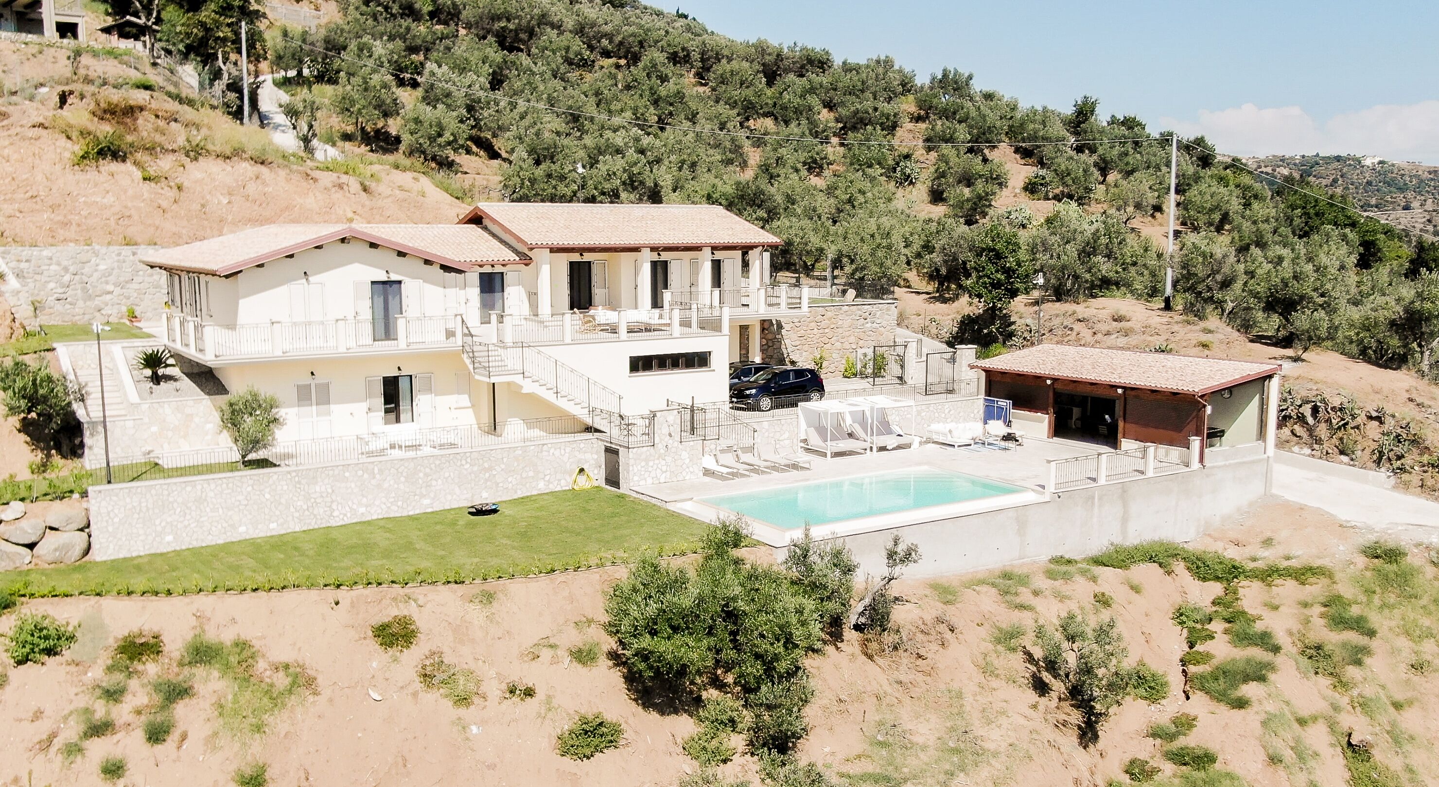 A two-story house with a swimming pool, a covered outdoor seating area, and a stone wall.