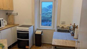 Cocina compacta con armarios de madera, microondas, estufa y ventana con vistas a árboles.