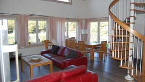 En rummelig opholdsstue med en rød lædersofa, et træspisebord og en spiraltrappe.