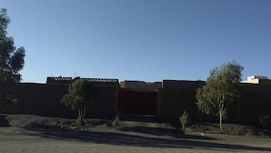 A building with a large open entrance, surrounded by trees and a dirt area. - Dar Lkhalifa Merzouga (Taouz)