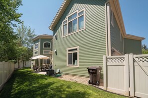 Una casa de dos pisos con fachada verde, patio trasero cercado y patio con mobiliario exterior.