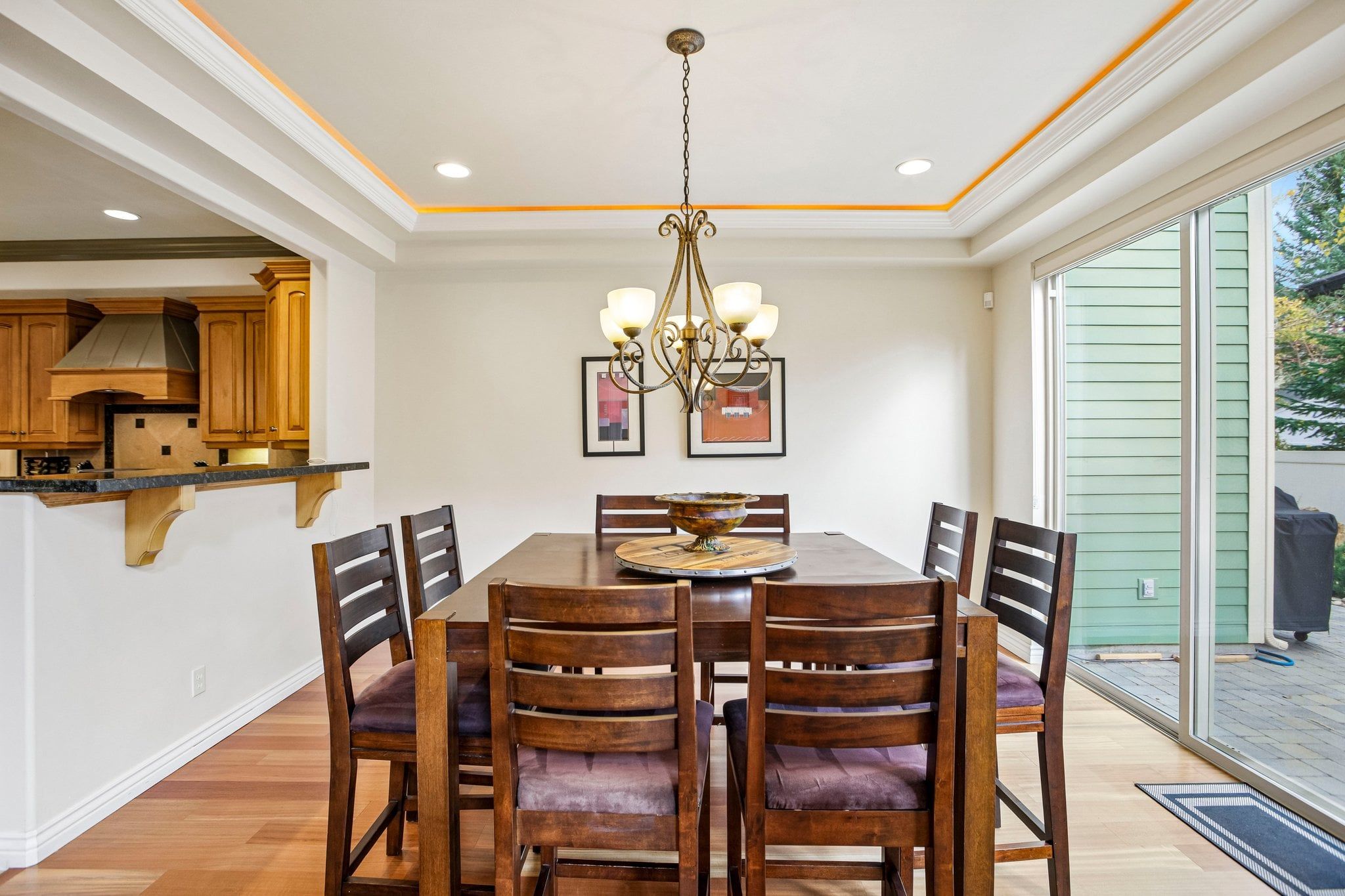 A dining area with a round table, wooden chairs, a chandelier, and a view to the outside.
