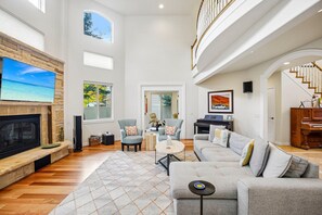 A spacious living room with a fireplace, comfortable seating, a piano, and a large TV.