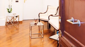 A room with a wooden floor, a white door, a white sofa, and a small table with a vase of flowers. - Magik Rooms (Rome)