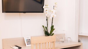 A compact workspace with a wooden chair, a small black refrigerator, a flat-screen TV, and a vase with white flowers. - Magik Rooms (Rome)